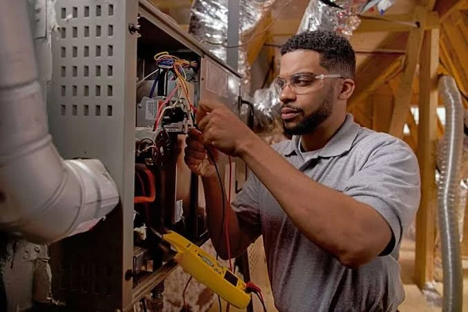 Heating technician inspecting wiring inside an open furnace
